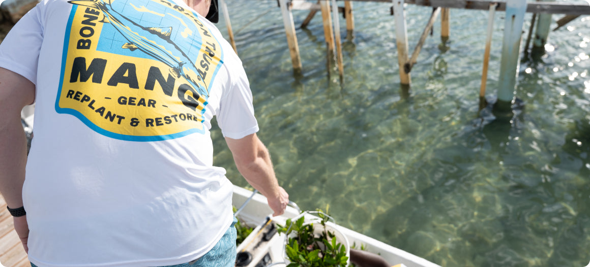 MANG volunteer in a MANG bonefish and tarpon design shortsleeve performance shirt delivering buckets of mangrove seedlings by boat