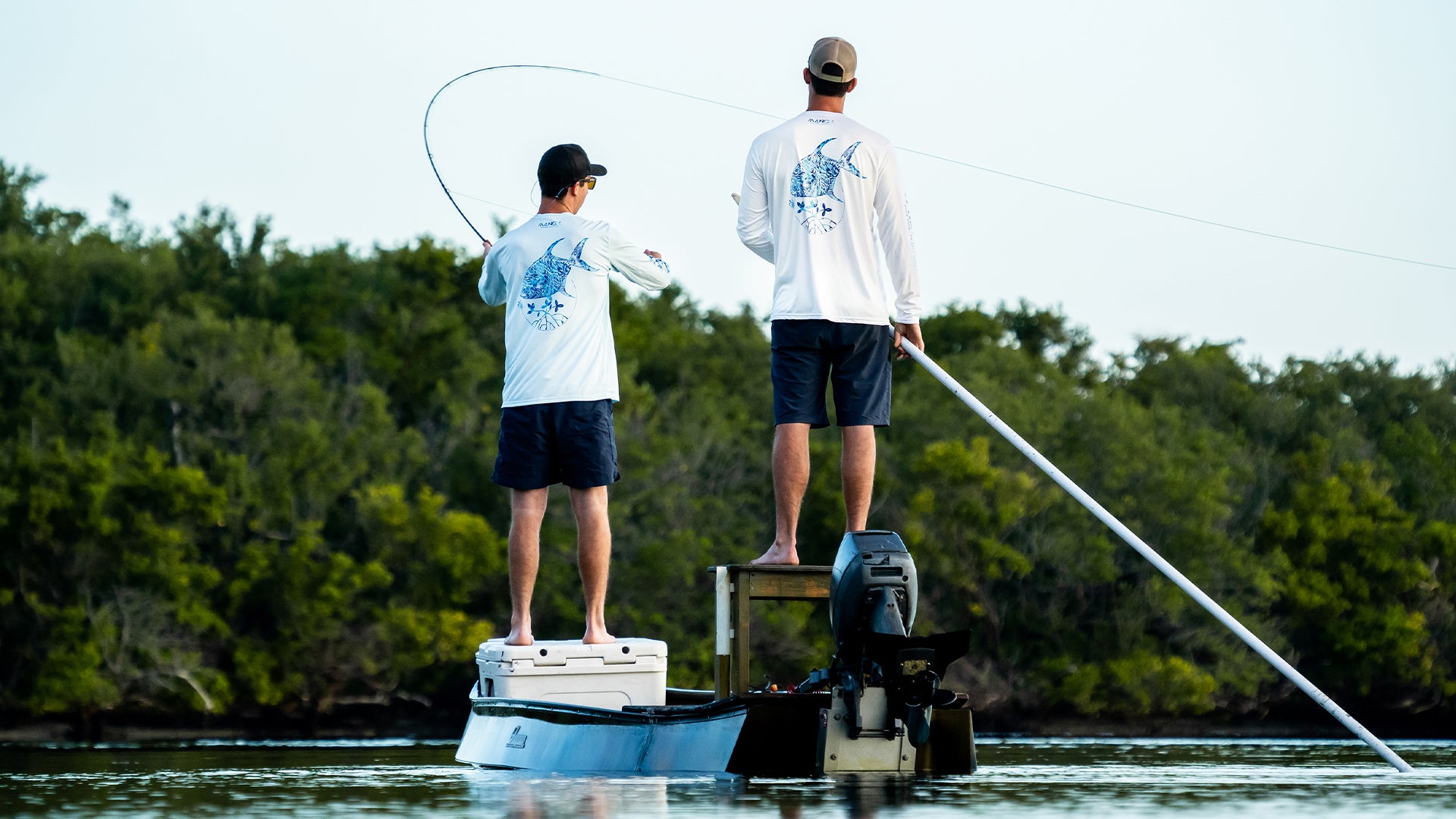 Two friends fishing together on a boat while wearing MANG longsleeve performance shirts