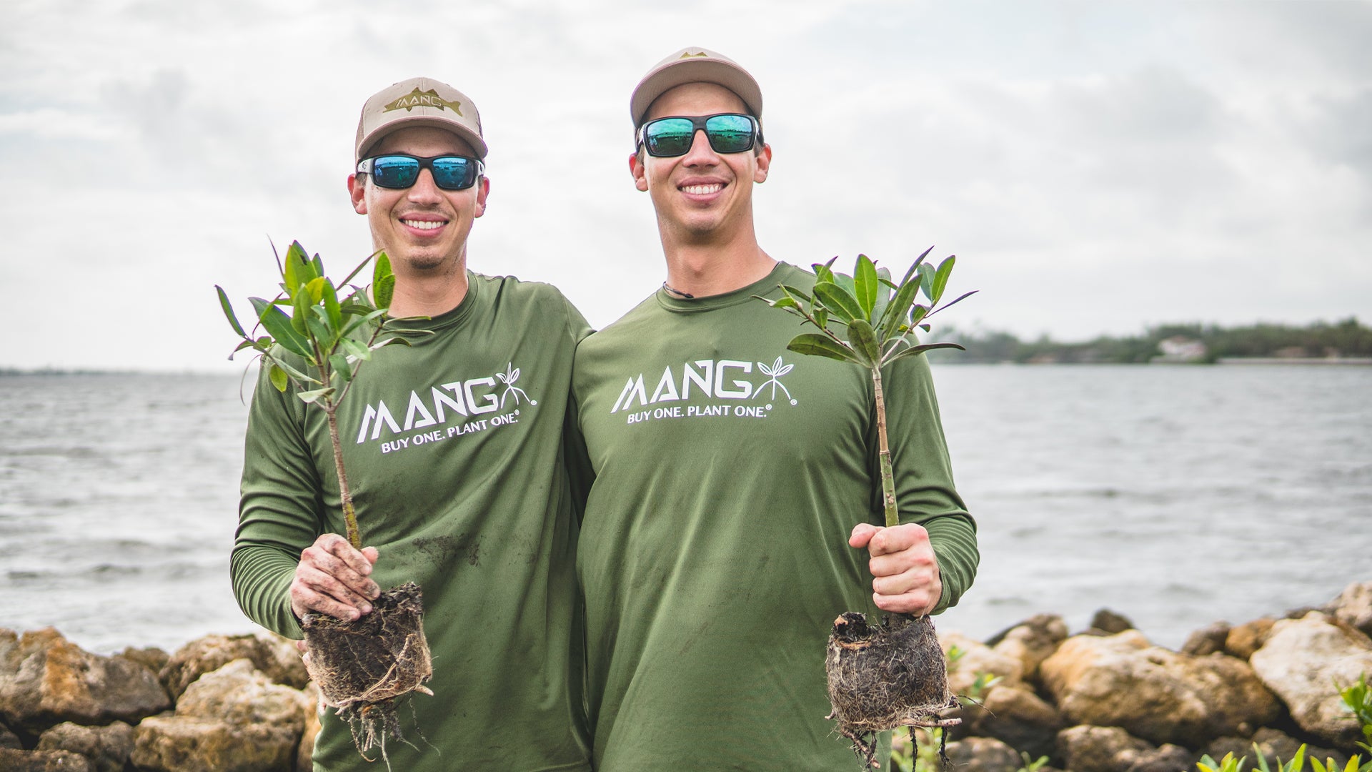 Keith and Kyle Rossin posing together for a photo while holding mangrove seedlings