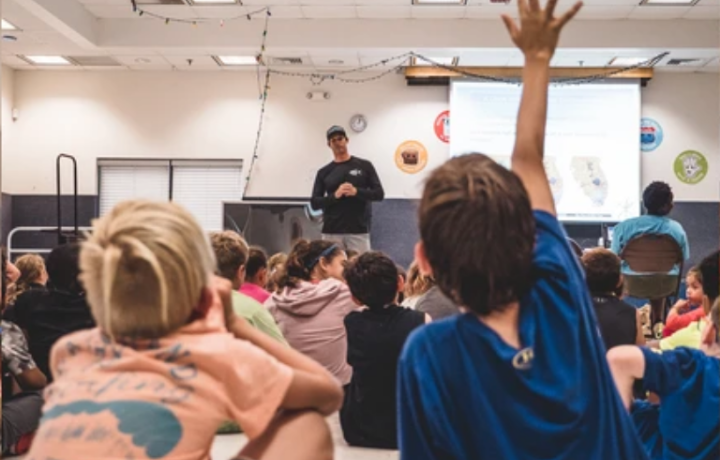 Child in classroom raising hand to ask a question to a mang education volunteer about mangrove restoration